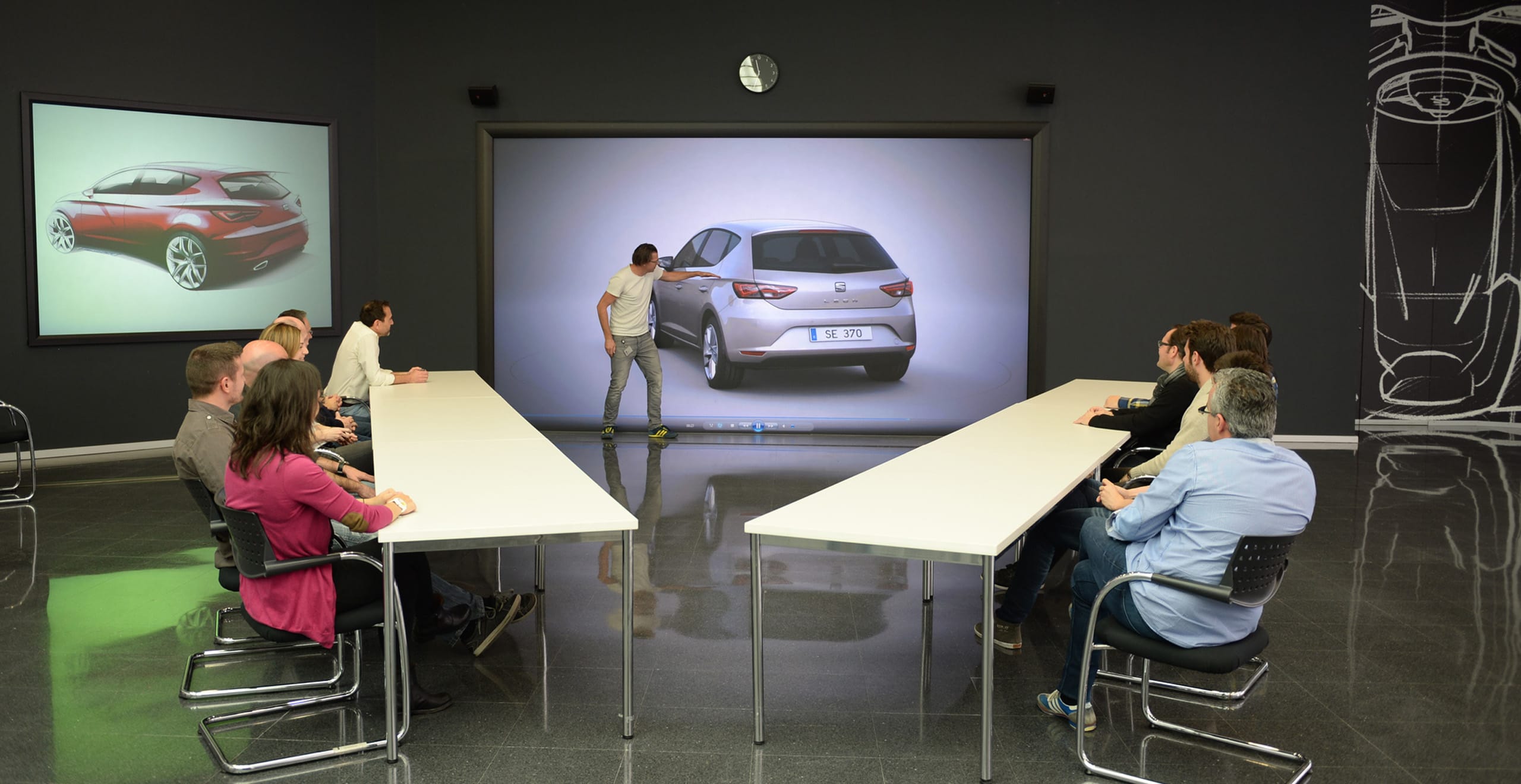 Ümarlaua arutelu, kus üks mees osutab SEAT Leoni kujundusele ja grupp laua taga istuvaid inimesi vaatab – SEAT tööandjana