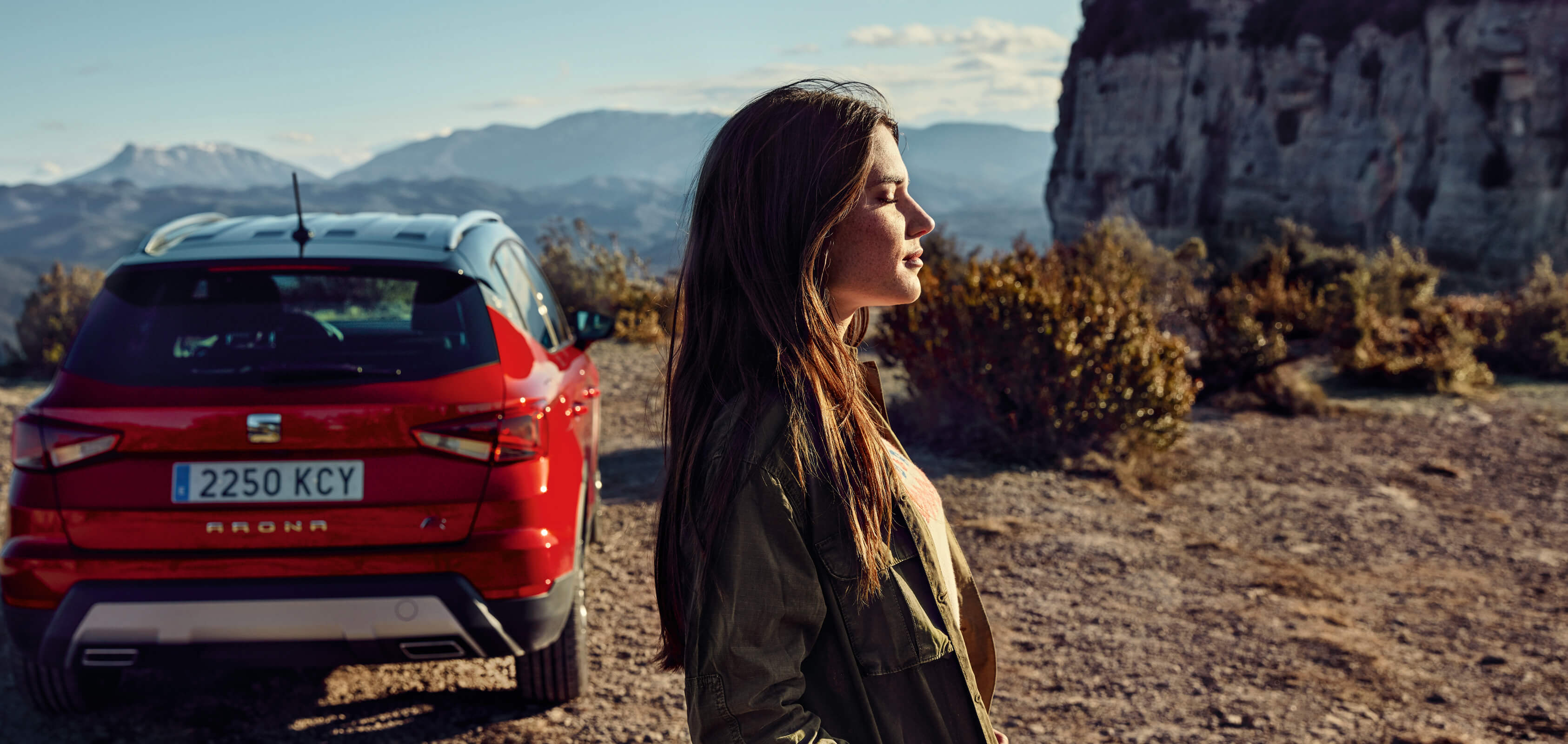 SEATi uute autode teenused – kõrbesse pargitud SEAT Arona crossover SUV tagantvaade koos naise profiilivaatega